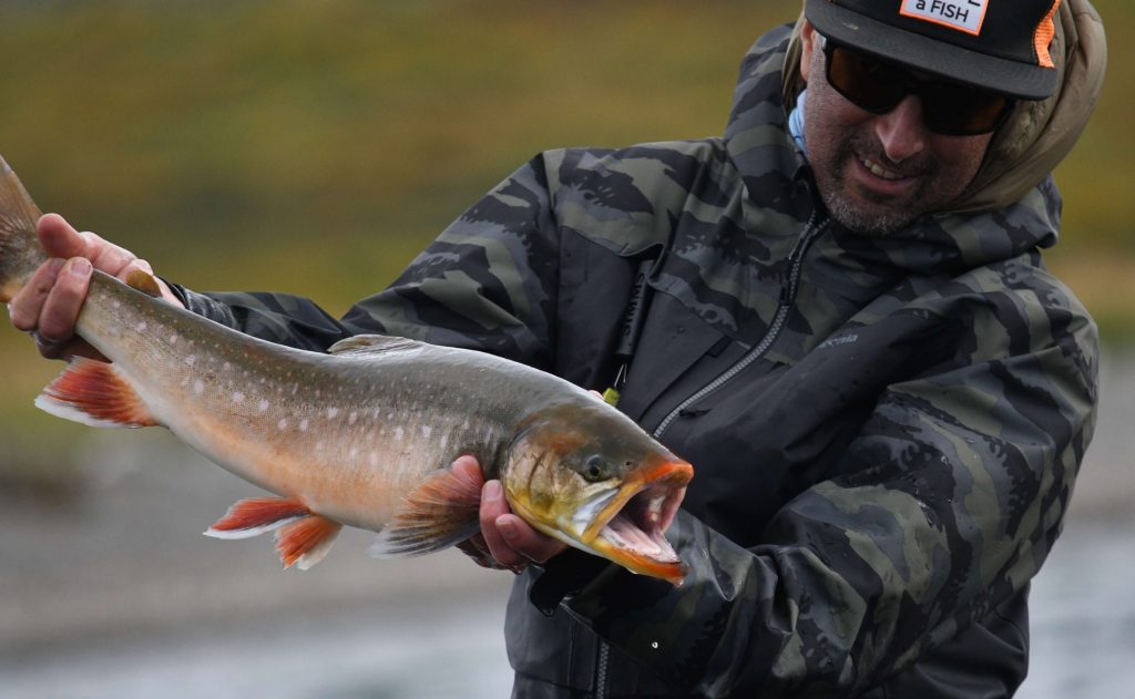 Fly angler holding a colorful char beside the river