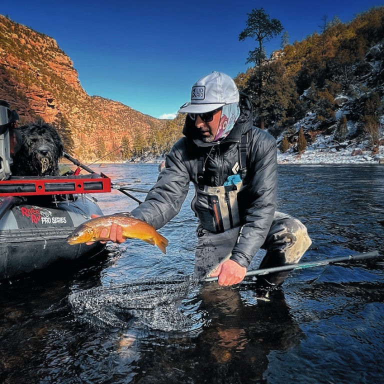 Angler kneeling in a canyon river, releasing a trout from the net